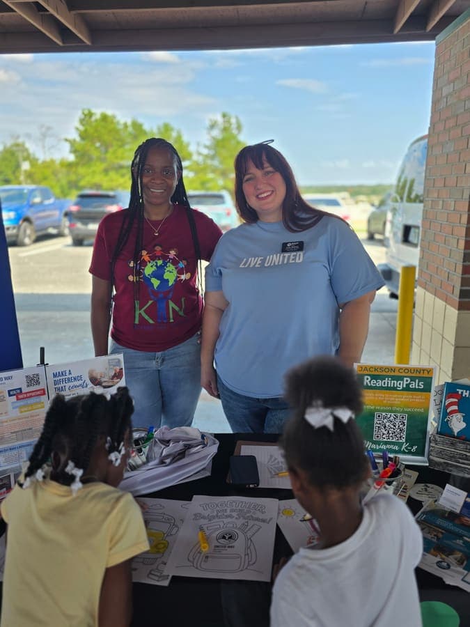 K.I.N. volunteer with a community partner at a resource table while kids play nearby
