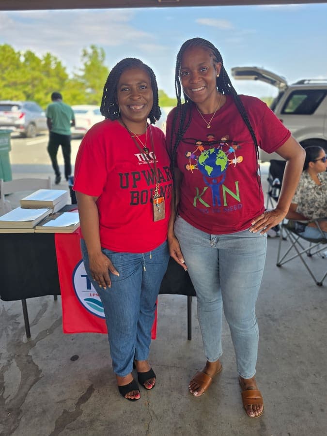 Two K.I.N. volunteers in K.I.N. shirts at a vendor table