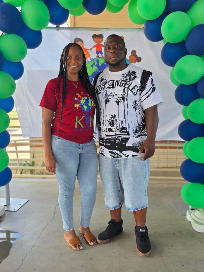 K.I.N. volunteer and a young man under the green and blue balloon arch