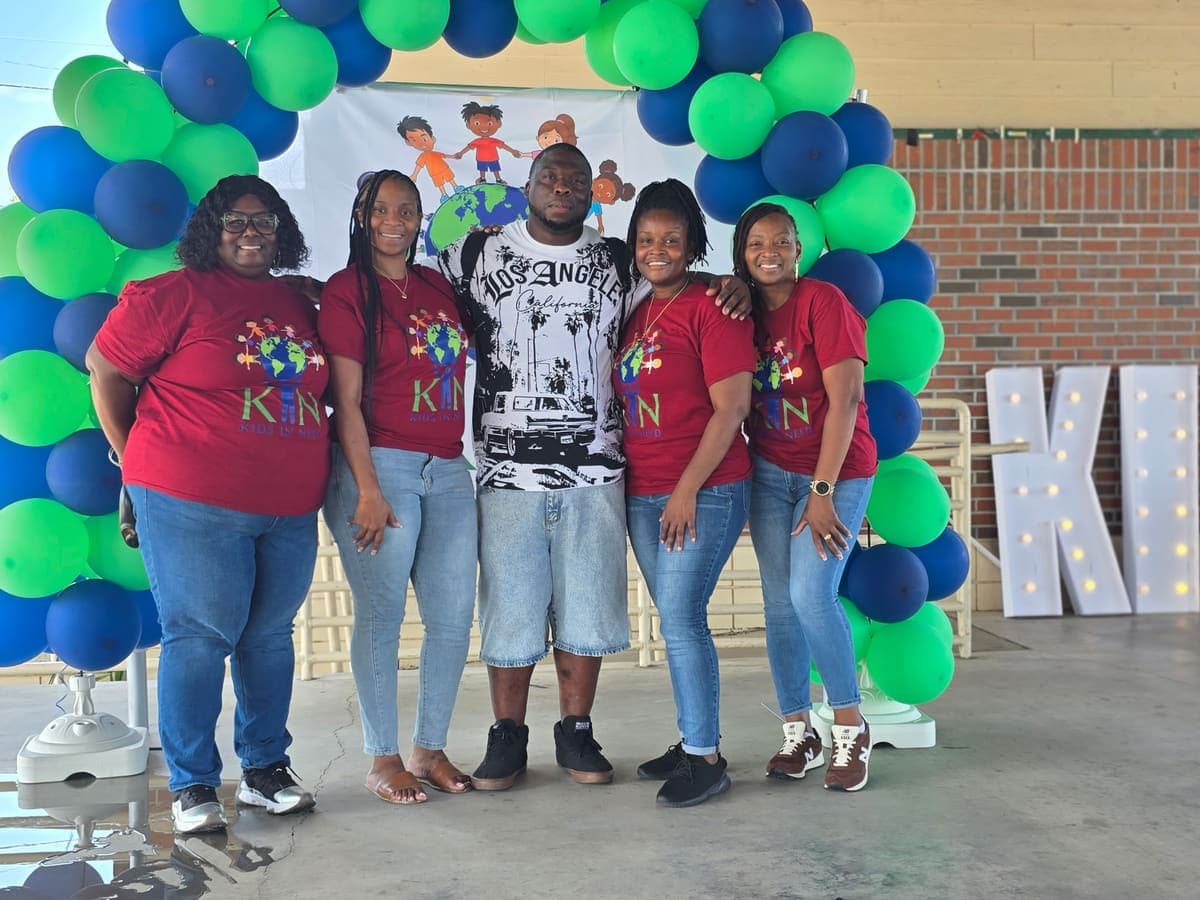 Group of K.I.N. volunteers and families posing under the balloon arch