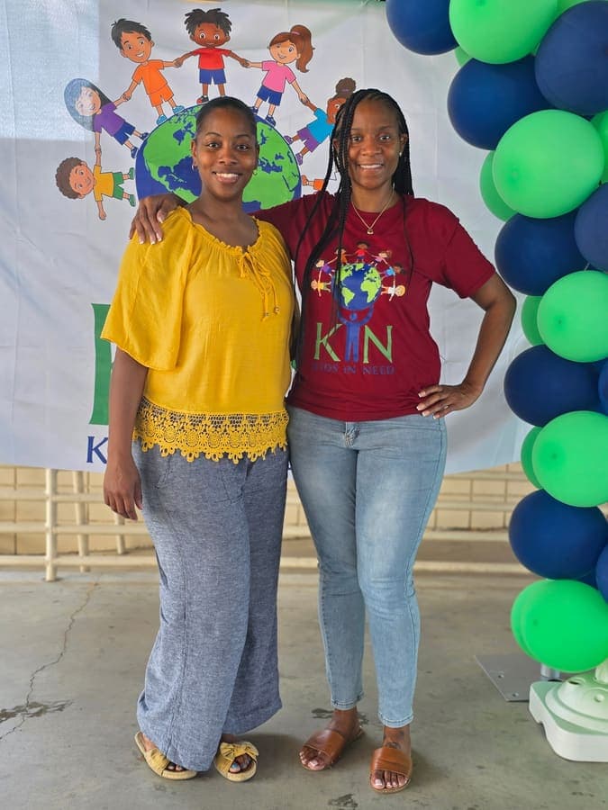 Two women smiling in front of the K.I.N. Kids In Need backdrop