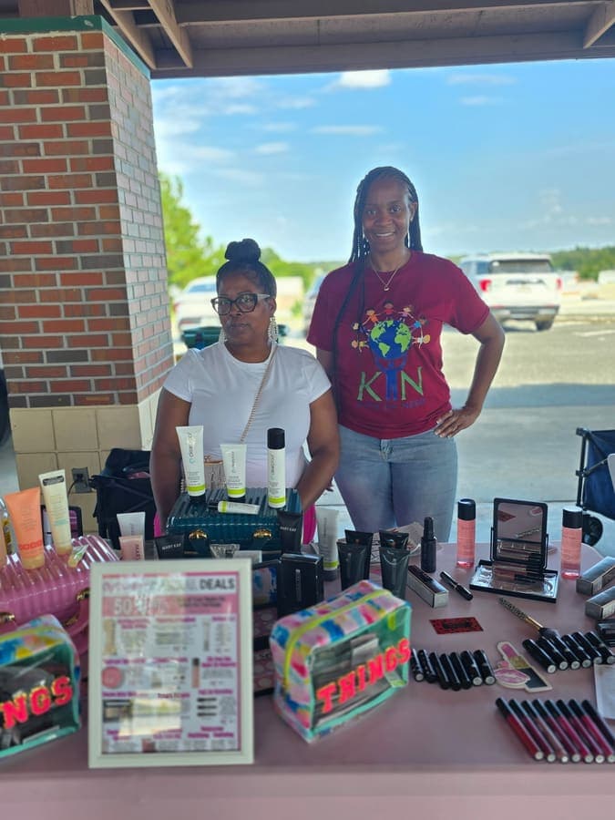 K.I.N. volunteer and a vendor at a cosmetics table