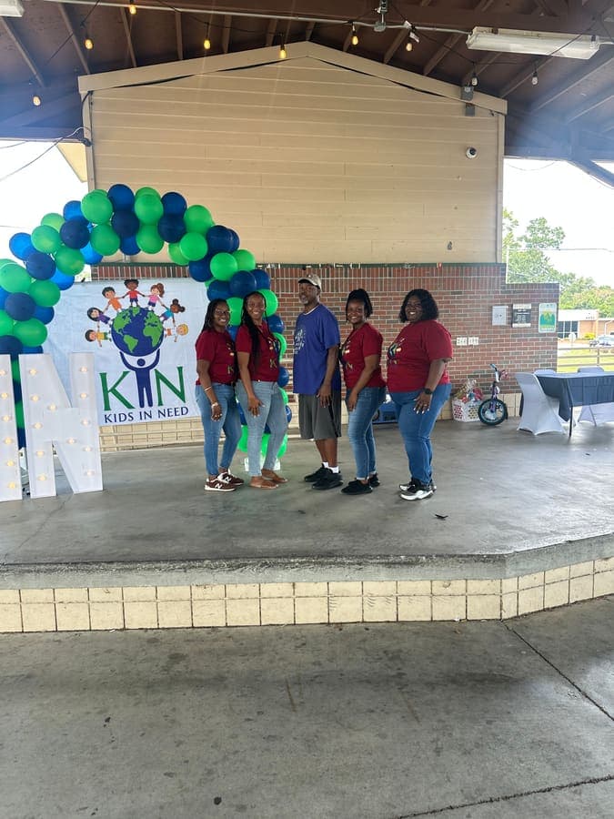 K.I.N. volunteers under the balloon arch next to large K.I.N. marquee letters