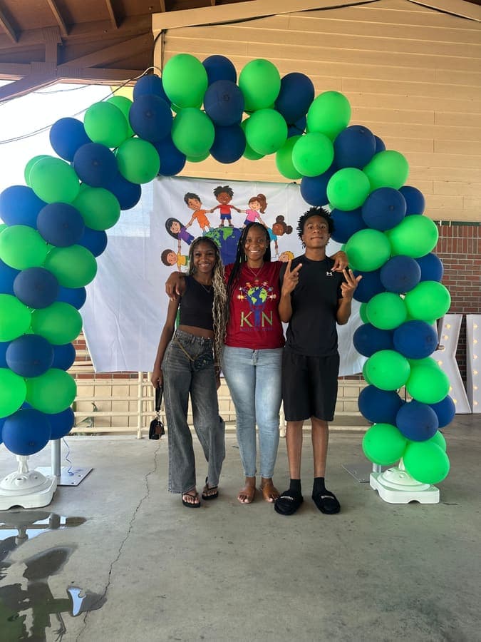Three young people posing under the balloon arch
