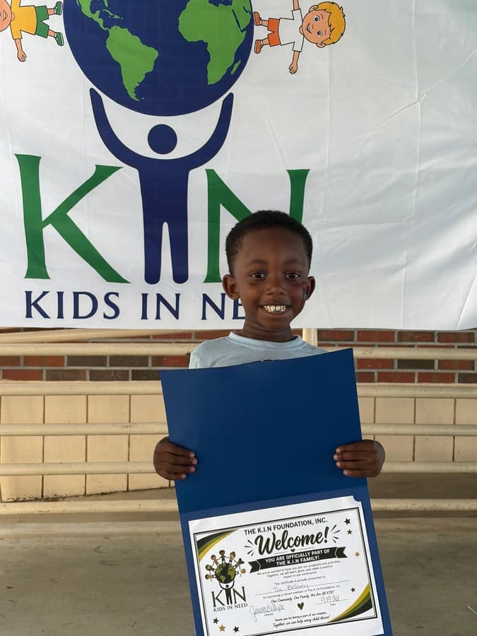 Smiling child holding a K.I.N. welcome certificate